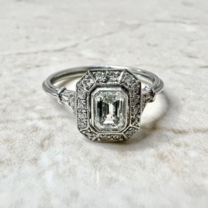 Puede incluir: Un anillo de compromiso de plata con un gran diamante talla esmeralda claro rodeado por un halo de diamantes m&aacute;s peque&ntilde;os.