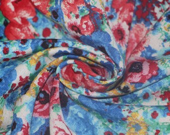 May include: Close-up of a floral fabric with a swirling pattern. The fabric features a mix of red, blue, and yellow flowers on a white background. The design is detailed and the fabric appears to be soft and lightweight.