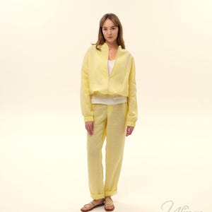 Op de afbeelding: Een lichtgele linnen jas met rits, gecombineerd met een bijpassende broek. De outfit wordt gedragen met een witte top en sandalen. De set is een casual, comfortabele stijl, perfect voor warm weer.