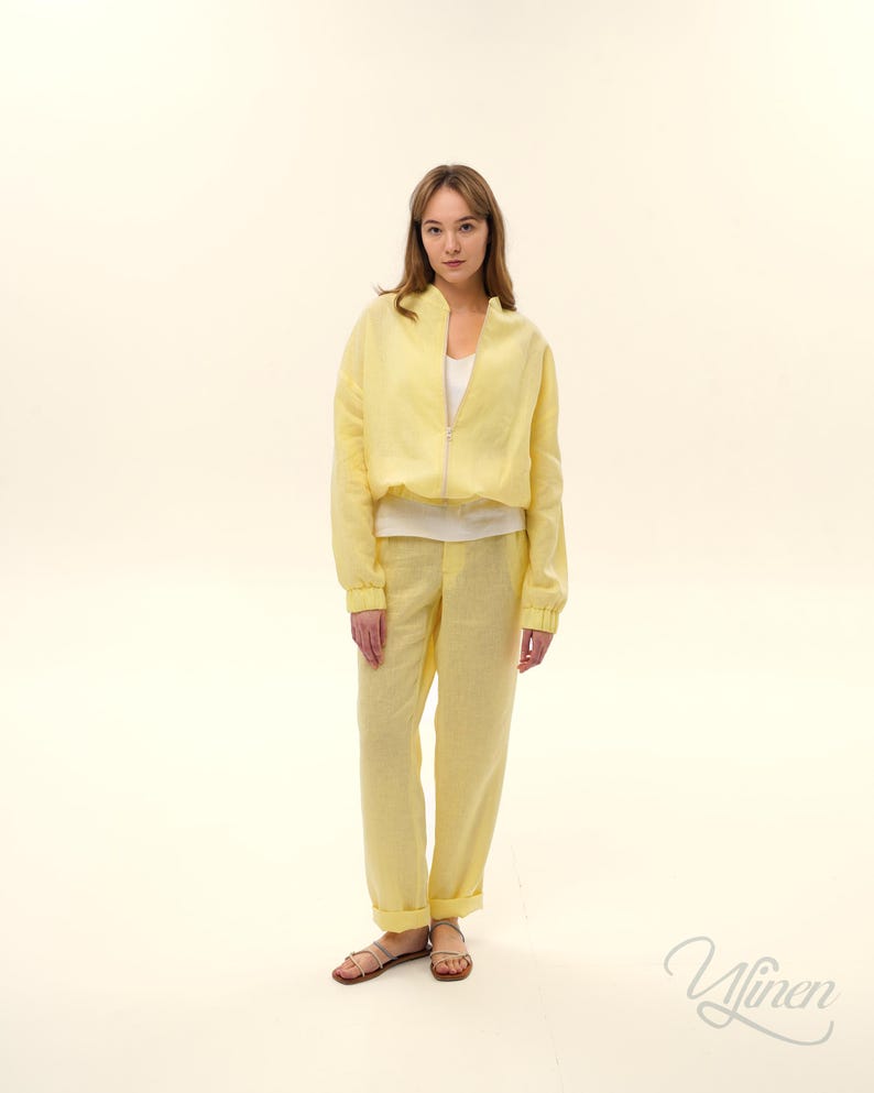 Op de afbeelding: Een lichtgele linnen jas met rits, gecombineerd met een bijpassende broek. De outfit wordt gedragen met een witte top en sandalen. De set is een casual, comfortabele stijl, perfect voor warm weer.