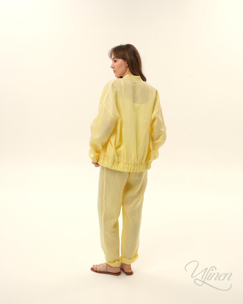 Op de afbeelding: Een lichtgele linnen tweedelige set, bestaande uit een jasje en een broek. Het jasje heeft een opstaande kraag en een elastische tailleband. De broek heeft omgeslagen enkels. De set is gemaakt van een lichte stof, ideaal voor warm weer.