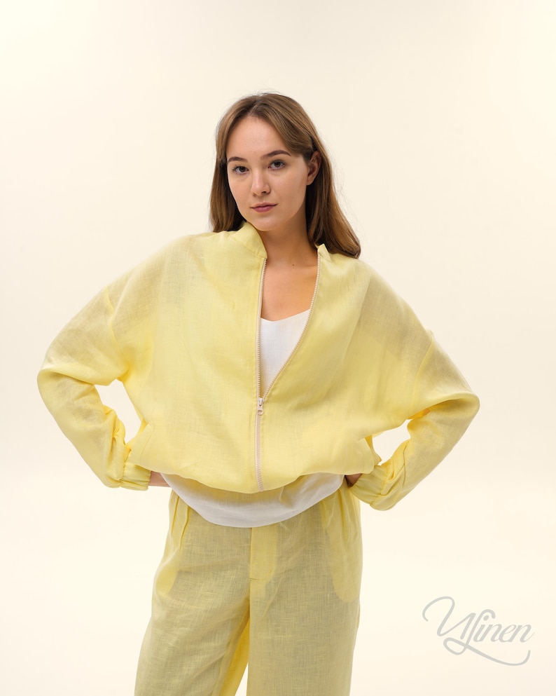 Op de afbeelding: Een lichtgele linnen jas met ritssluiting, gecombineerd met een bijpassende broek. De jas heeft een relaxte pasvorm en lange mouwen. De outfit is gemaakt van een lichte stof, perfect voor warmer weer. De jas is ongeveer 61 cm lang.
