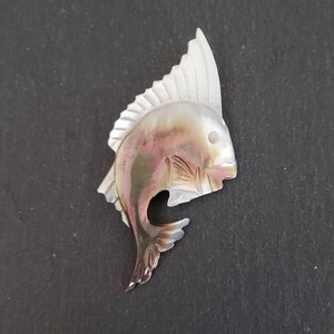 May include: A carved iridescent mother of pearl fish pendant with a white dorsal fin. The fish is facing to the right and has a detailed design.
