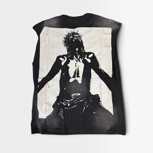 Könnte beinhalten: Ein schwarzes ärmelloses Shirt mit einem kontrastreichen, weißen Grafikdruck einer Figur mit Dornenkrone, ausgestreckten Armen und nach oben geneigtem Kopf. Das Design ist auf einem rechteckigen Hintergrund zentriert.