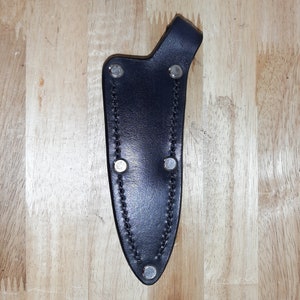 Può includere: Un fodero per coltello in pelle nera con rivetti argentati e un bordo cucito.