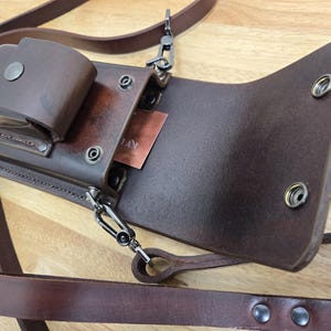 May include: A brown leather phone case with a flap and a strap. The case has a metal clasp and several metal rivets. The case is open and the inside is visible.