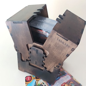 May include: A wooden card box with a hinged lid, open to reveal a stack of cards. The box is decorated with a carved design and the inscription "VASILY39".