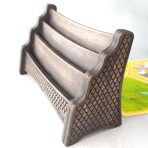 May include: A wooden card holder with three slots, featuring a decorative dragon scale pattern on the side. The holder is stained a dark brown color.