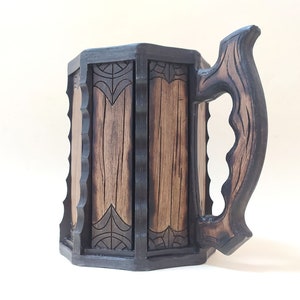 May include: A dark brown wooden beer stein with a carved handle and intricate designs. The stein has a hexagonal shape and is made of wood.