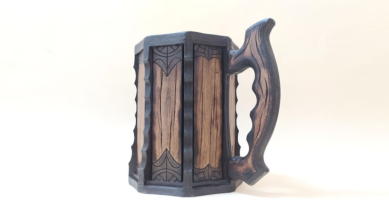 May include: A dark brown wooden beer stein with a carved handle and intricate designs. The stein has a hexagonal shape and is made of wood.
