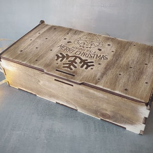 May include: A wooden box with a hinged lid. The lid is decorated with a laser-cut design of a snowflake and the text "Wishing you a Merry Christmas".