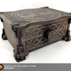 May include: A dark brown wooden box with a single drawer, featuring laser-cut Celtic knotwork patterns on the front and a tree design on the lid. A circular knob with a triskelion symbol is centred on the drawer front. The box has four feet.