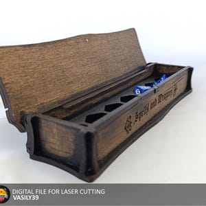 May include: A wooden box with a hinged lid, designed to hold dice. The box has a compartment for each die and is engraved with the text "The 5 Spells and the Mystery of the"