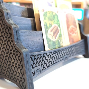 May include: A wooden card holder with a black finish and a decorative pattern. The holder has three slots for cards and a raised base.