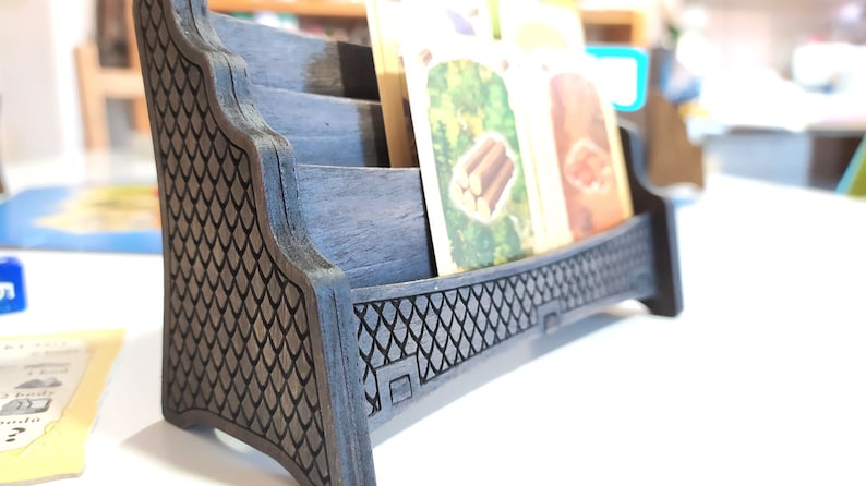 May include: A wooden card holder with a black finish and a decorative pattern. The holder has three slots for cards and a raised base.