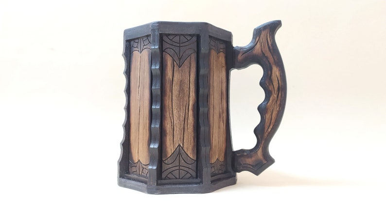 May include: A wooden beer stein with a dark brown finish and intricate carvings. The handle is shaped like a branch and has a textured surface.