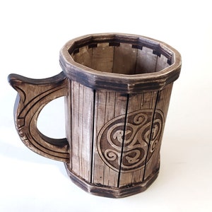 May include: A wooden mug with a Celtic knot design. The mug is brown and has a handle.