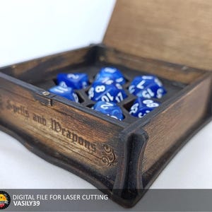 May include: A wooden box with a hinged lid, engraved with the words "Spells and Weapons". The box is open and contains a set of blue dice.