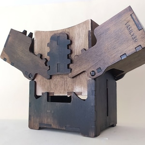 May include: A wooden box with a hinged lid and a unique interlocking design. The box is stained a dark brown color and has the text "VASILY39" engraved on the side.