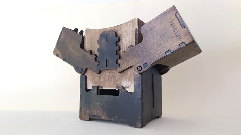 May include: A wooden box with a hinged lid and a unique interlocking design. The box is stained a dark brown color and has the text "VASILY39" engraved on the side.