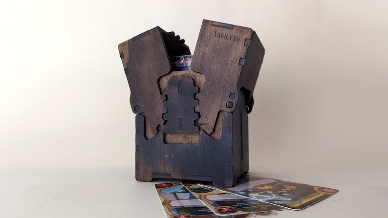 May include: A wooden box with a hinged lid, the lid is open and the box is empty. The box is stained a dark brown color and has a black finish. The box is labeled "VASILY39". There are several playing cards on the table in front of the box.