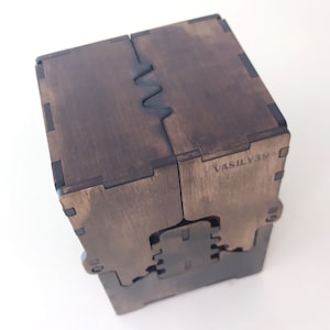 May include: A dark brown wooden box with a unique interlocking design. The box is made of multiple pieces of wood that fit together seamlessly. The box has a label on the side that reads "VASILY39".