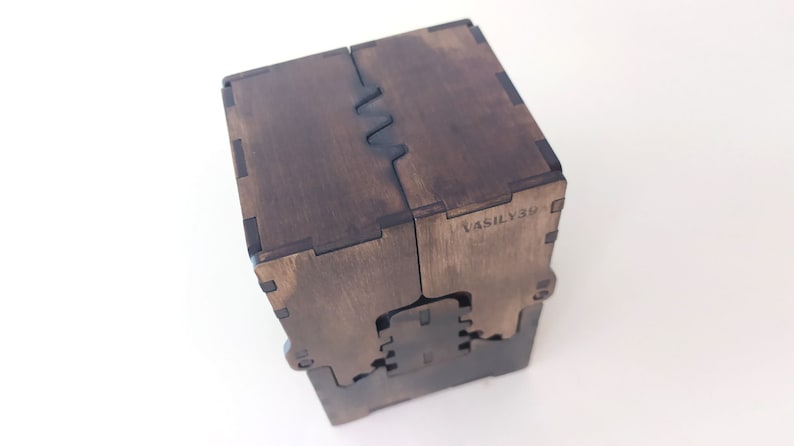 May include: A dark brown wooden box with a unique interlocking design. The box is made of multiple pieces of wood that fit together seamlessly. The box has a label on the side that reads "VASILY39".