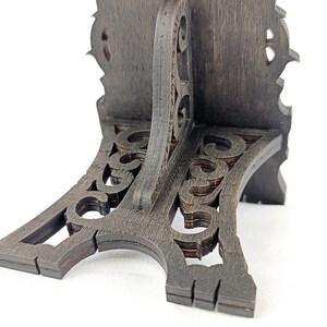 May include: A dark brown, wooden decorative stand with an ornate, carved design. The stand has a curved base with openwork detailing and a vertical support with a decorative top. The stand is on a white background.
