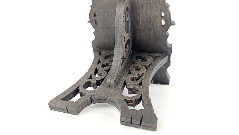 May include: A dark brown, wooden decorative stand with an ornate, carved design. The stand has a curved base with openwork detailing and a vertical support with a decorative top. The stand is on a white background.
