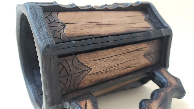 May include: A wooden mug with a dark brown stain and intricate carvings. The mug has a handle and a base with carved feet. The mug is made of wood and has a rustic look.