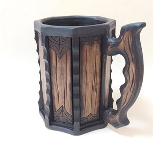 May include: A wooden beer stein with a dark brown finish and intricate carvings. The stein has a large handle and a wide mouth.