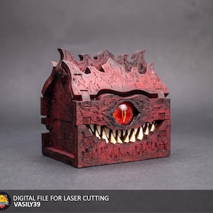 Peut inclure: Une boîte en bois rouge foncé avec un œil rouge brillant au centre et une rangée de dents blanches pointues. La boîte présente une surface texturée complexe avec des motifs de flammes sculptés sur le couvercle. Texte en bas : DIGITAL FILE FOR LASER CUTTING VASILY39.
