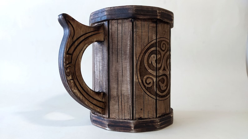 May include: A wooden beer stein with a dark brown finish. The stein has a carved handle and a Celtic knot design on the front.