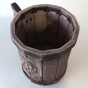 May include: A wooden mug with a dark brown finish and a carved design. The mug has a handle and a wide, octagonal opening.