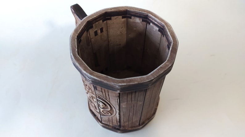 May include: A wooden mug with a dark brown finish and a carved design. The mug has a handle and a wide, octagonal opening.