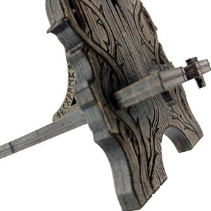 May include: A wooden wine bottle stopper holder with a decorative, carved design. The holder is gray with a detailed wood grain pattern and a horizontal bar to hold the bottle stopper. The design includes a carved floral pattern.