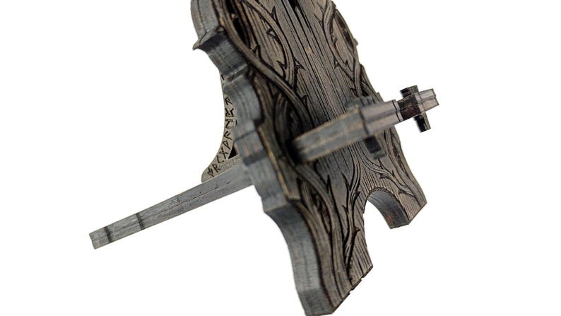 May include: A wooden wine bottle stopper holder with a decorative, carved design. The holder is gray with a detailed wood grain pattern and a horizontal bar to hold the bottle stopper. The design includes a carved floral pattern.
