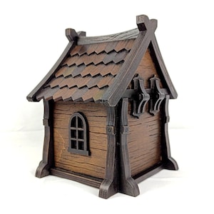 May include: A small, brown, wooden-style house model featuring a dark brown shingled roof, vertical support beams, and a single arched window on the side. The structure has a textured finish resembling wood grain and a peaked roof design.