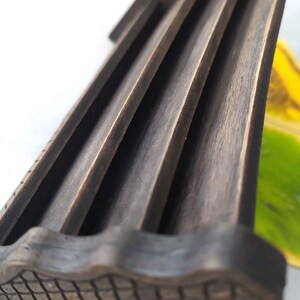 May include: Close-up of a wooden game piece with a grooved top and a textured bottom. The piece is dark brown and appears to be part of a board game.