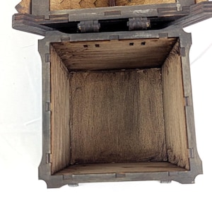 May include: A square wooden box with dark brown stained surfaces and visible interlocking finger joints at the corners. The box is open, revealing a hollow interior with a natural wood grain texture and a hinged lid attached at the top edge.