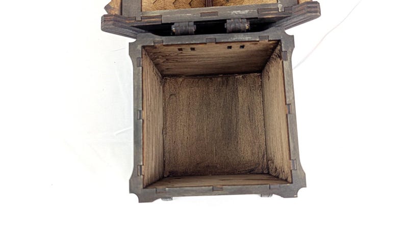 May include: A square wooden box with dark brown stained surfaces and visible interlocking finger joints at the corners. The box is open, revealing a hollow interior with a natural wood grain texture and a hinged lid attached at the top edge.