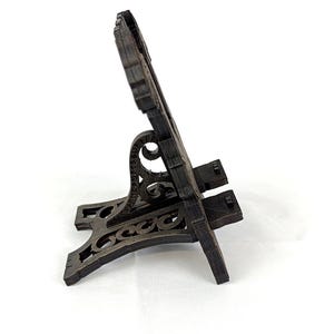 May include: A dark brown wooden phone stand with an ornate design. The stand has a decorative base and a back with a carved pattern. The stand is designed to hold a phone or small tablet.