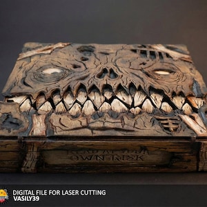 May include: A detailed wooden box with a carved skull-like face on the lid. The box is brown with white teeth and glowing eyes. The text "READ AT OWN RISK" is carved on the front. Digital file for laser cutting.