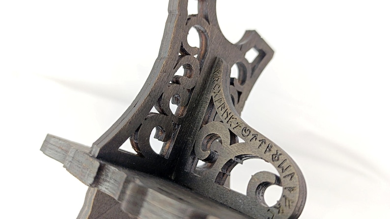 May include: Close-up of a dark brown wooden shelf bracket with intricate cut-out designs and text. The bracket has a decorative, ornate style, with a sturdy base and angled support. The wood grain is visible.