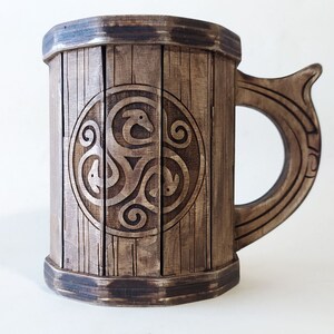 May include: A wooden beer stein with a dark brown finish. The stein features a carved Celtic knot design on the front. The handle is also carved with a Celtic knot design.