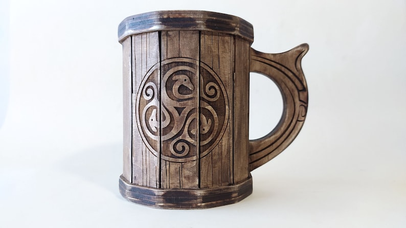 May include: A wooden beer stein with a dark brown finish. The stein features a carved Celtic knot design on the front. The handle is also carved with a Celtic knot design.