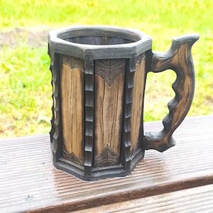 May include: A wooden beer stein with a dark brown finish and intricate carvings. The stein has a handle and a hexagonal shape.