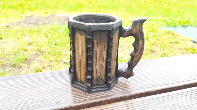 May include: A wooden beer stein with a dark brown finish and intricate carvings. The stein has a handle and a hexagonal shape.