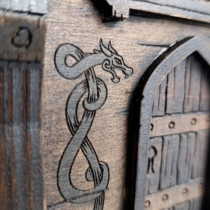 May include: A dark brown wooden structure featuring an arched door with vertical planks and a keyhole. The exterior surface is decorated with an engraved dragon design that wraps around the door frame. The wood grain is visible throughout.
