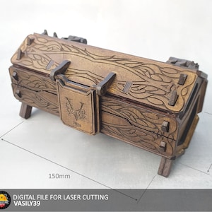 Op de afbeelding: Een houten doos met een scharnierend deksel en ingewikkelde houtsnijwerk. De doos is 150 mm lang en 70 mm breed. Het deksel heeft een decoratief metalen slot met een gestileerde letter "V" en de tekst "VASILY39".